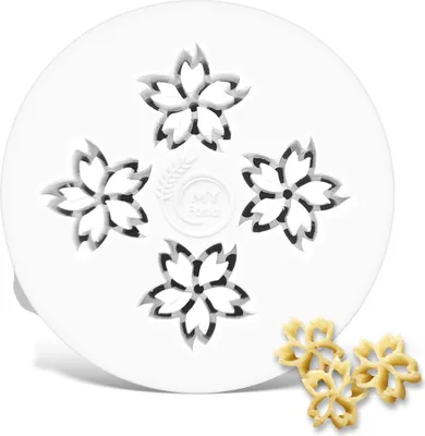 A white pasta maker attachment with a cherry blossom pattern, with two finished pasta shapes in the foreground.