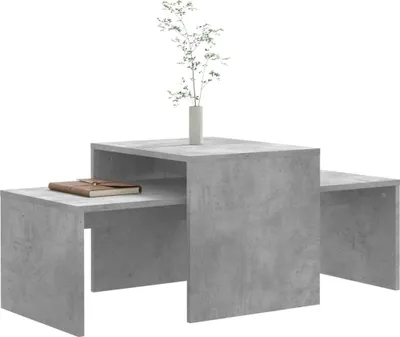 A set of three nesting coffee tables with a concrete-like finish, displayed on a white background. A small vase with a plant is placed on the largest table.