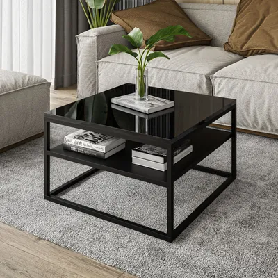 A modern living room scene with a black glass-top coffee table in the foreground, placed on a gray rug. A sofa and a pouf are visible in the background.