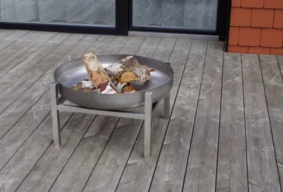A metal fire pit with logs sits on a wooden deck.