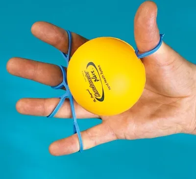 A hand is holding a yellow therapy ball with blue elastic bands around the fingers and thumb.