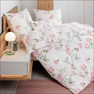 A close-up view of a bed with floral patterned bedding, a bedside table with a lamp, and a rug.
