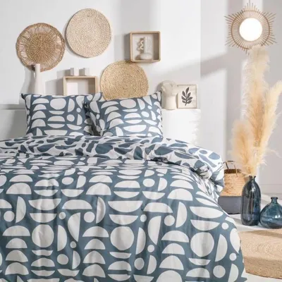 A bedroom scene with a bed dressed in a patterned duvet cover and pillows, decorated with wall art and decorative items.