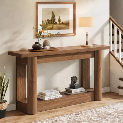 A wooden console table with decorative items and books is placed in a hallway next to a staircase.
