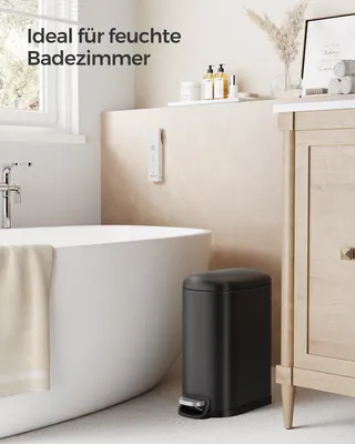A modern bathroom with a bathtub, a black pedal trash can, and a wooden vanity.