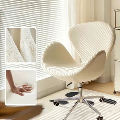 A cream-colored chair with a modern design is placed in a room with natural light streaming through blinds.