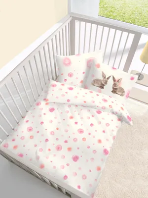 A baby crib with bedding featuring a pink polka dot pattern and two cartoon bunnies.