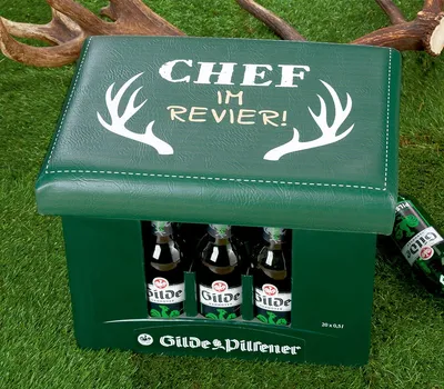 A green cooler box with beer bottles inside, placed on a grassy surface with deer antlers in the background.