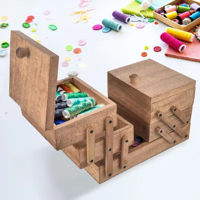 A wooden sewing box with various spools of thread and buttons scattered around it on a white surface.