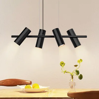 A modern black metal pendant light fixture with three adjustable spotlights hangs above a wooden table with a bowl of fruit and a vase with flowers.