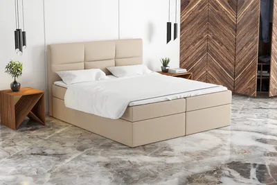 A beige boxspring bed with white bedding is shown in a room with marble flooring and a wooden wardrobe in the background.