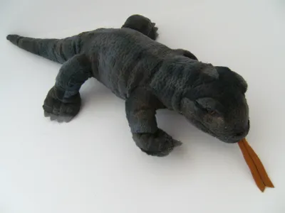 A plush toy Komodo dragon lying on a white surface.