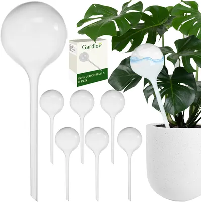 A set of white plant watering globes is displayed alongside a potted plant, with a box of the product in the background.