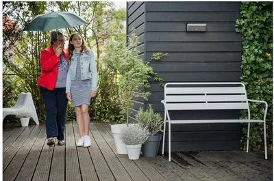 Two people walking under an umbrella on a wooden deck next to a modern house.