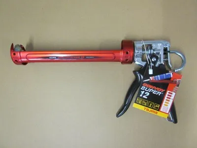A red caulking gun with a black handle and a product tag attached, lying on a light brown background.