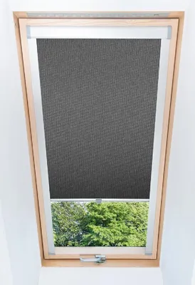 A close-up view of a dark gray blackout roller blind installed in a wooden-framed skylight window.