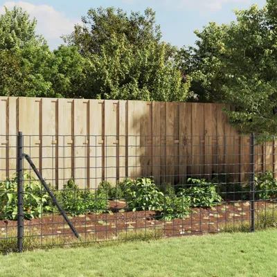 A wire mesh fence in front of a wooden fence, with plants and grass in the foreground and background.