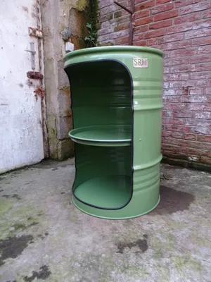 A green barrel repurposed into a shelf unit, placed outdoors on a concrete floor next to a brick wall and a weathered door.