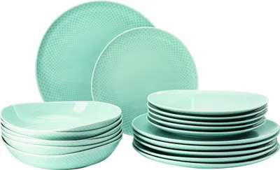 A set of light green ceramic plates and bowls are neatly stacked against a white background.