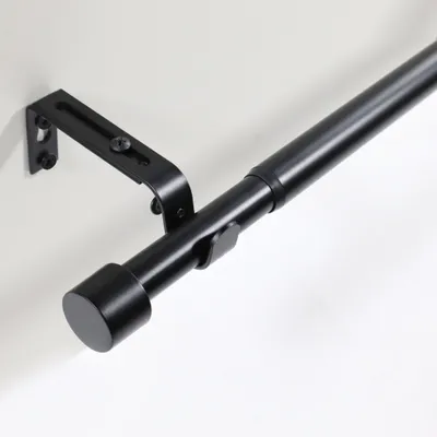 Close-up of a black adjustable curtain rod mounted on a white wall.