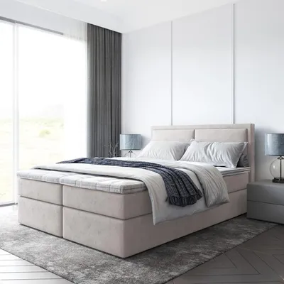 A modern bedroom with a beige upholstered box spring bed, grey curtains, and a large window.