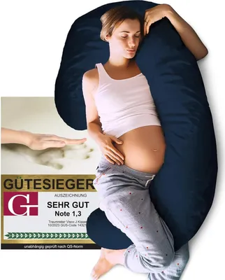 A pregnant woman is sleeping comfortably, embracing a large navy blue side sleeper pillow. A certification badge is visible in the lower left corner.