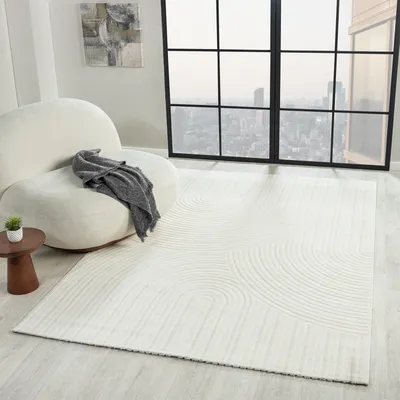 A modern living room with a white armchair, a small side table with a plant, and a large window overlooking a city skyline. A white rug with a wave pattern is laid out on the floor.