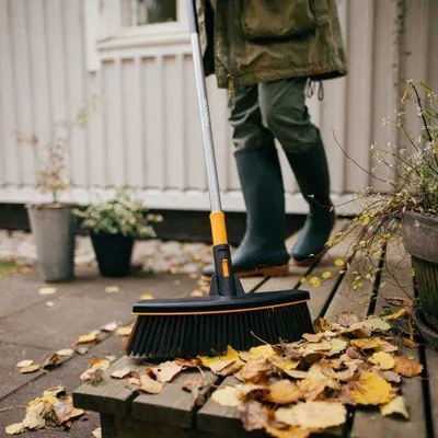 A person is sweeping fallen leaves from a wooden deck with a broom.