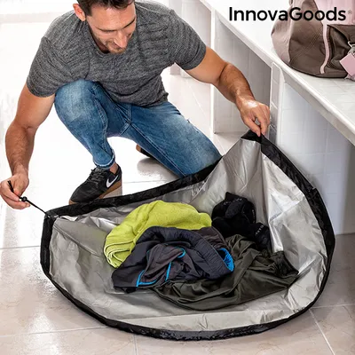 A man is crouching and putting clothes into a large, circular mat that is also a bag.