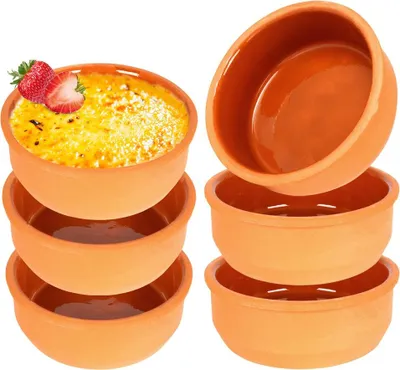 A set of terracotta ramekins, one filled with crème brûlée and topped with strawberries, stacked against a white background.