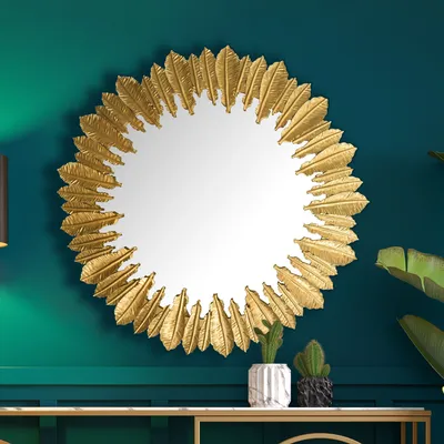 A decorative round mirror with a gold, feather-like frame is displayed on a dark green wall above a console table.