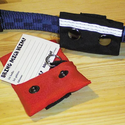 A red and black dog collar accessory with an attached information card is shown on a wooden surface.