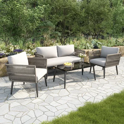 A four-piece outdoor furniture set on a stone patio surrounded by greenery.