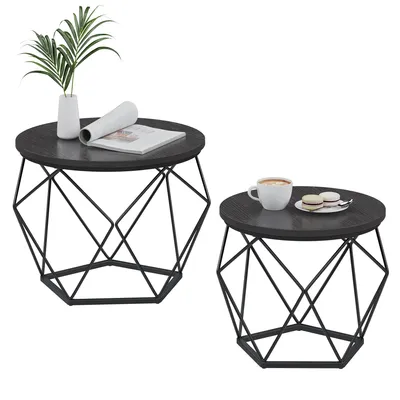 Two round coffee tables with geometric metal bases and dark wood tops, one set with a plant and book, the other with a coffee cup and macarons.