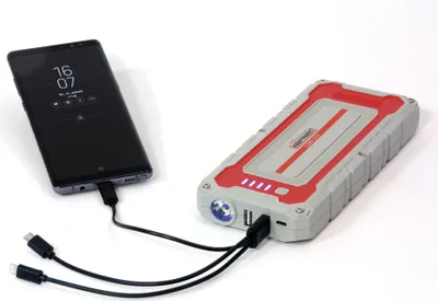 A black smartphone is connected to a red and gray power bank with cables.
