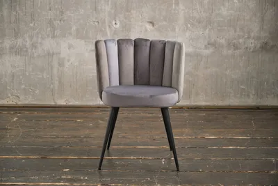 A gray velvet dining chair with black legs is shown against a concrete wall and wooden floor.