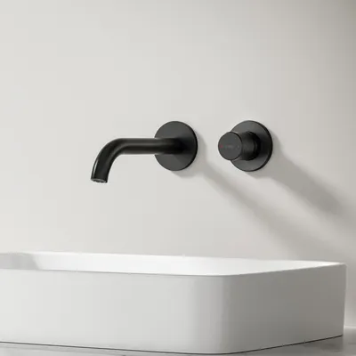 A black wall-mounted faucet and control knob are installed above a white rectangular sink against a white wall.