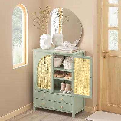 A light green shoe cabinet with cane doors and drawers, placed in a hallway next to a window and a door.