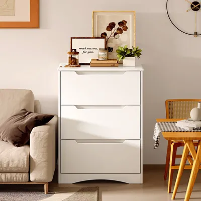 A white dresser with decorative items on top, next to a sofa and a chair with a table.