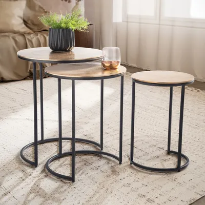 Three nesting tables with gold tops and black metal frames are arranged on a rug in a living room setting.