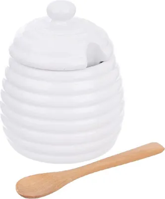 A white ceramic honey pot with a lid and a wooden spoon.