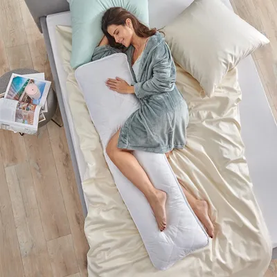A woman is sleeping on a bed with a long body pillow.