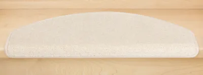A cream-colored, semi-circular stair mat placed on a light-colored wooden stair tread.