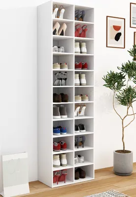 A tall, white shoe rack filled with various shoes, standing against a white wall next to a potted plant.