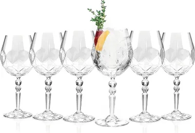 A set of six crystal cocktail glasses, with one glass filled with ice, fruit slices, and a sprig of greenery.