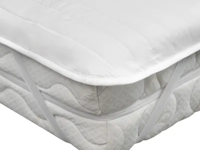 A close-up view of a white quilted mattress protector with elastic straps on a mattress.