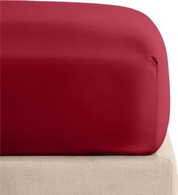 A close-up view of a red fitted sheet on a beige mattress.