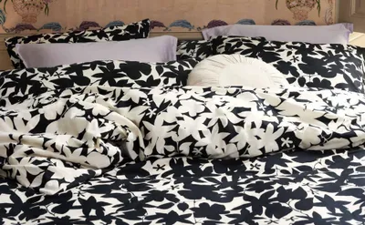A close-up view of a bed with black and white floral patterned bedding and light purple pillows.