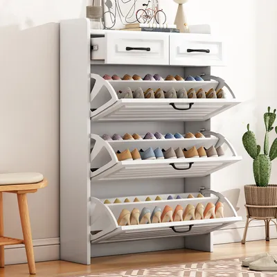 A white shoe rack with multiple shelves filled with shoes, positioned next to a small wooden stool. A potted cactus is visible on the right side of the image.