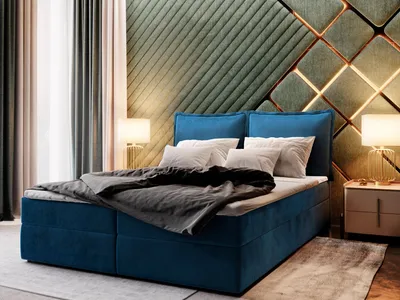 A bedroom scene featuring a blue boxspring bed with a dark gray comforter and white pillows. The headboard is a decorative green upholstered panel with gold accents. Lamps are on either side of the bed, and curtains are visible in the background.